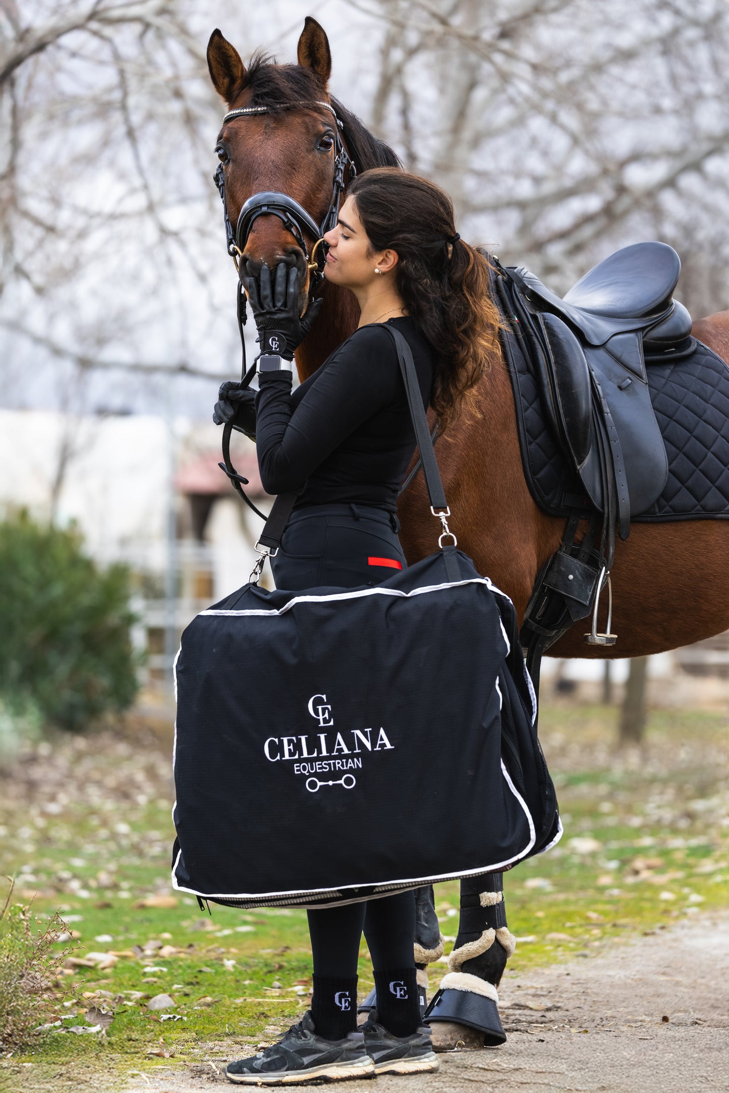 Jinete con bolsa funda para silla de montar negra Celiana Equestrian junto a su caballo - accesorios ecuestre premium