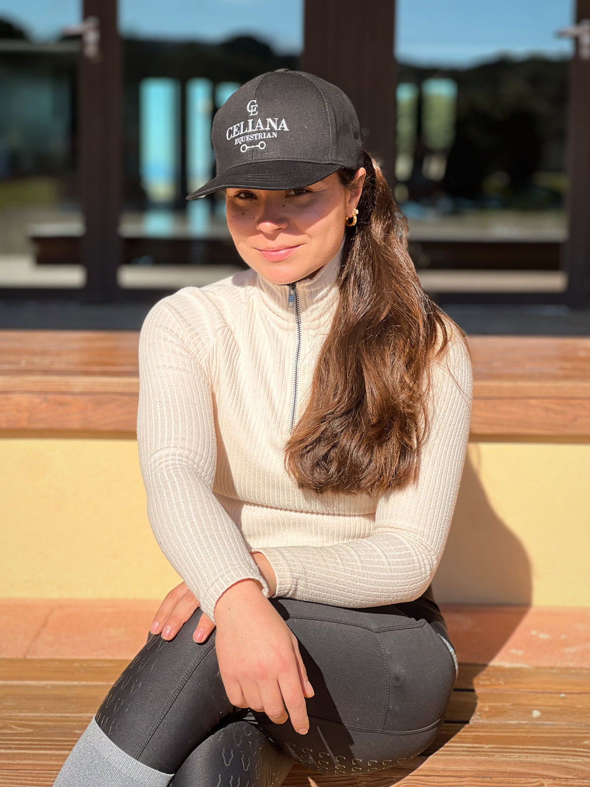 Amazona sentada con gorra ecuestre negra Celiana Equestrian bordada y leggings de equitación