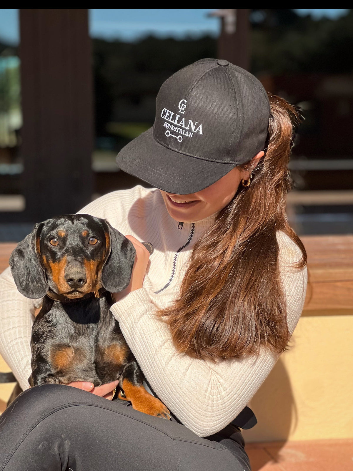 Amazona con gorra ecuestre negra Celiana Equestrian con logo bordado, junto a su perro teckel