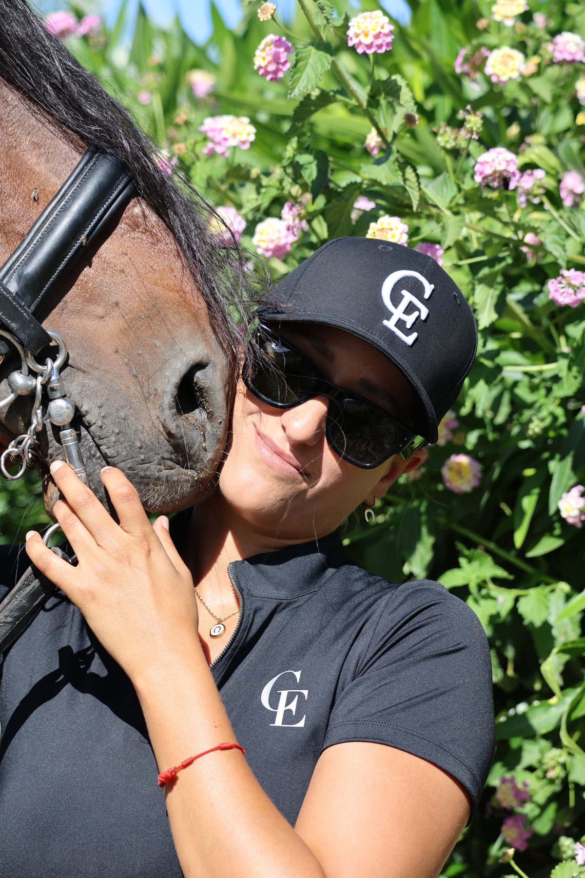 Amazona con gorra ecuestre negra Celiana Equestrian con logo CE y polo técnico, junto a su caballo