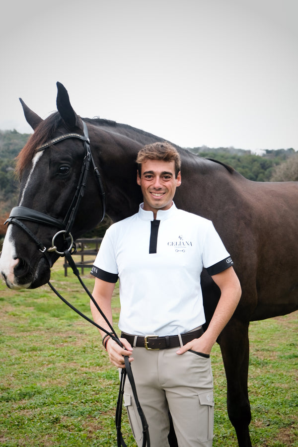 Jinete sonriente con polo de equitación blanco Celiana Equestrian junto a caballo negro, en exteriores