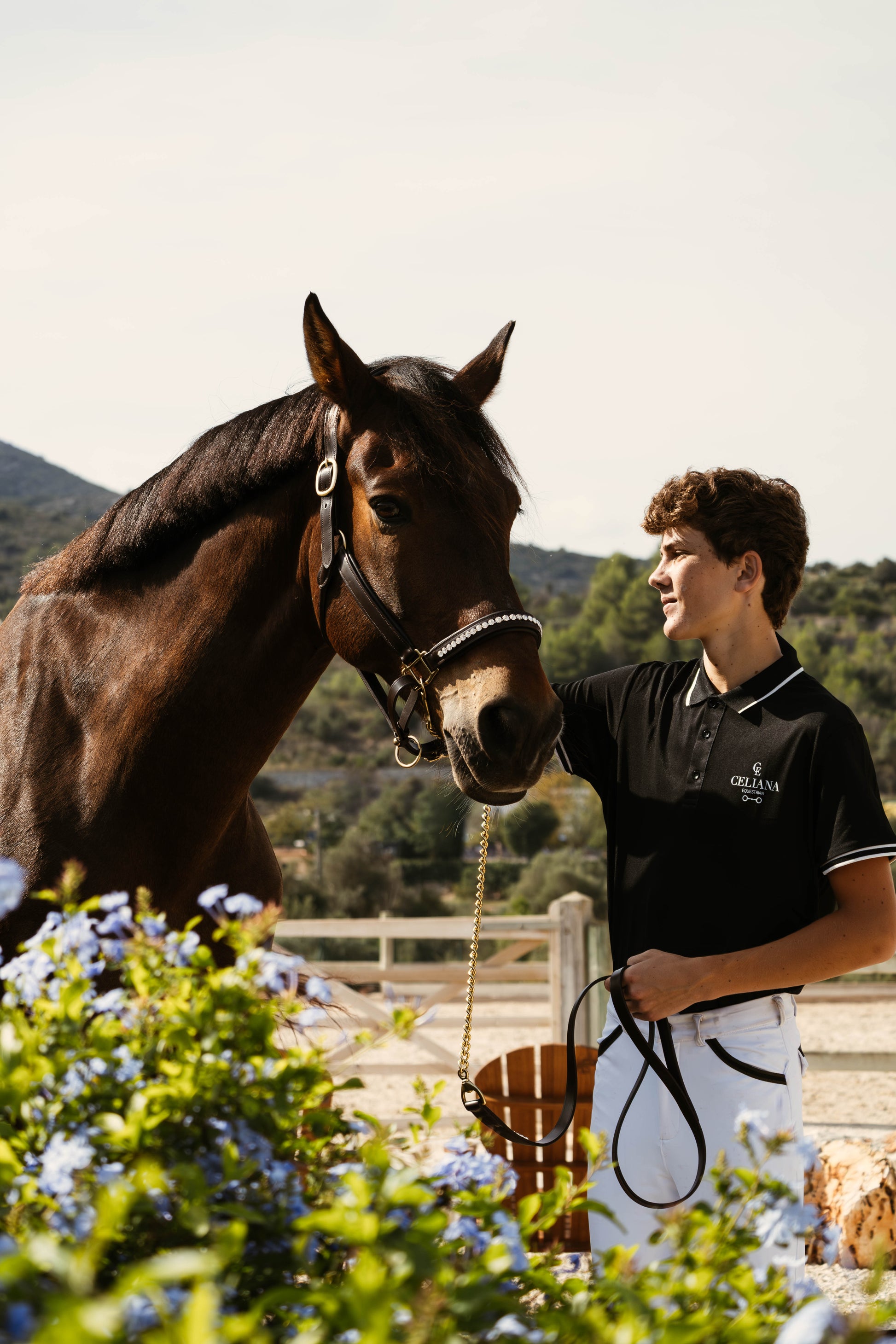 Polo de equitación negro Celiana Equestrian puesto en jinete junto a caballo en paddock