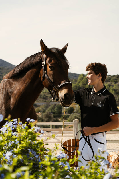 Polo de equitación negro Celiana Equestrian puesto en jinete junto a caballo en paddock