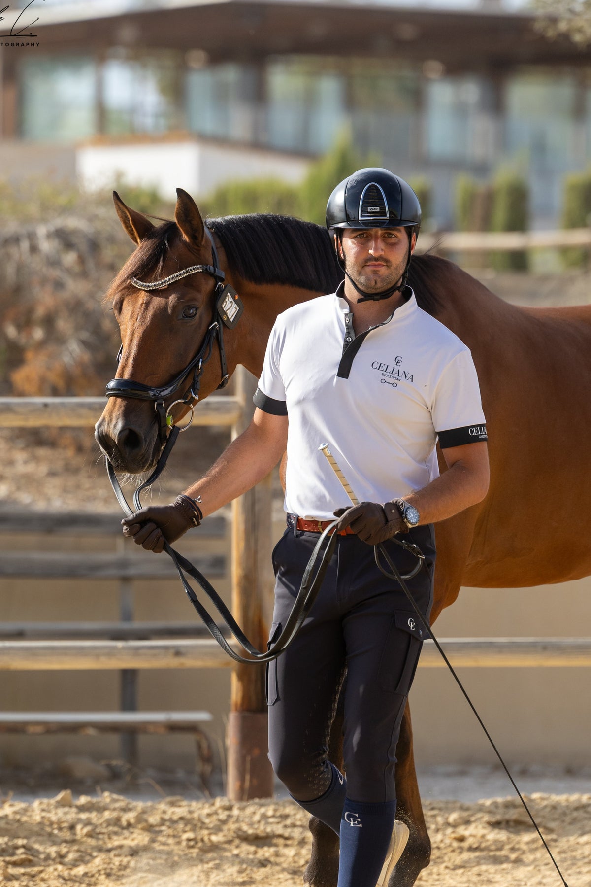 Jinete con Royal Stable Polo blanco de hombre Celiana Equestrian y pantalón de equitación azul marino, junto a su caballo castaño